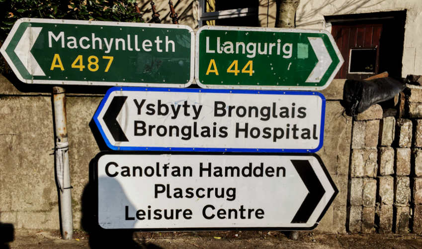 Primary route signs and a bilingual local sign in rural Wales.