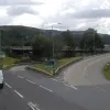 Beyond the unusual merge, there is a very short weaving space before the road splits into three. To the left, two lanes take the A58 climbing out of the town; to the right, two lanes climb over the middle of the roundabout to join the westbound Burdock Way across the viaduct, and down the middle, one lane vanishes into the undergrowth around the roundabout. Above it, a temporary metal-framed flyover connects the westbound A58 to the viaduct.