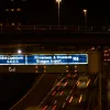 After dark, the direction signs really show their value. Not all look quite as clear as this one, though: they are still being manufactured and this one is almost brand new. You can make out the pattern of lighting tubes behind the sign face.
