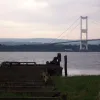 The supports for the pier continue out into the water, and beyond it, the structure that killed off the ferry arches across the river.