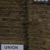 Further east, Union Street has another number plate, but this time in white on black. In the 1920s, A-roads were signed in black on white, B-roads in white on black. This sign could be anything up to eighty years old.  Photo by Tony