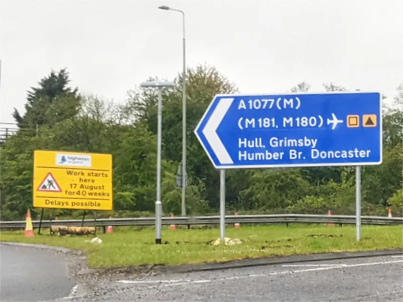 The direction sign standing opposite also shows the new designation, and makes clear that this road now leads to the M181, but no longer carries that number.